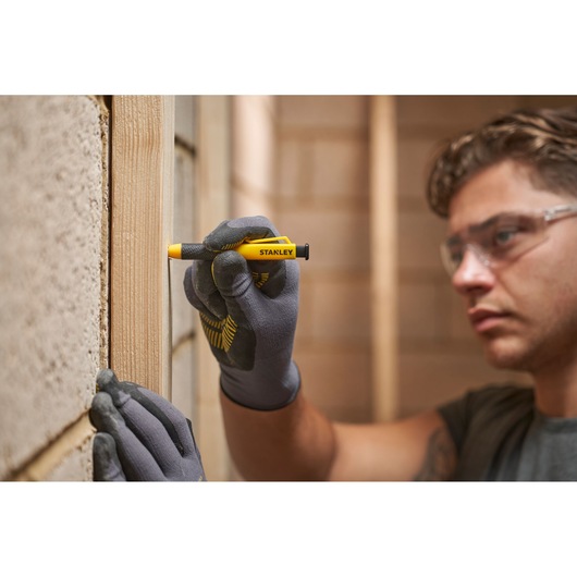 Person wearing gloves using a Stanley carpenter pencil to mark a wooden beam indoors.