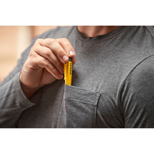 Hand placing a yellow STANLEY tool in the chest pocket of a grey shirt.