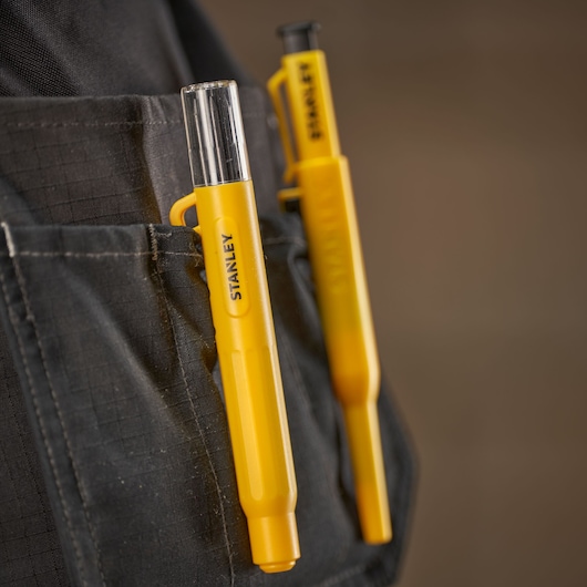 Two yellow STANLEY markers clipped to a pocket on dark fabric, shown in close-up detail.