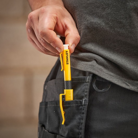 Hand placing a yellow Stanley tool in a pocket, tool features a clip and branding.
