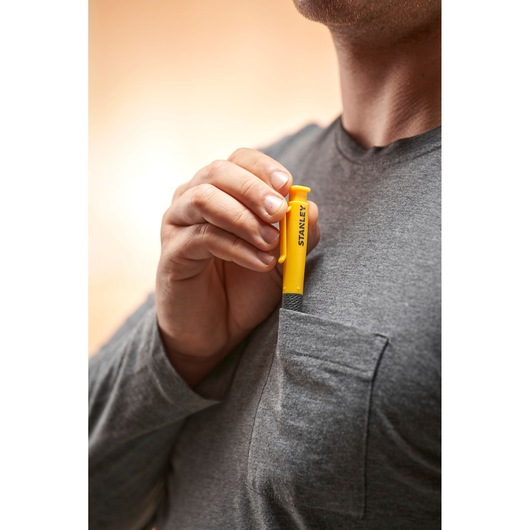 Person putting a yellow Stanley tool into the chest pocket of a grey shirt.