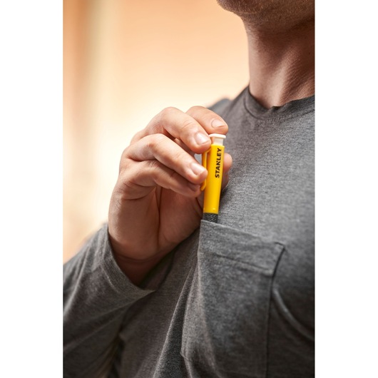 Person placing a yellow STANLEY tool in a gray shirt pocket, tool held upright with visible branding.