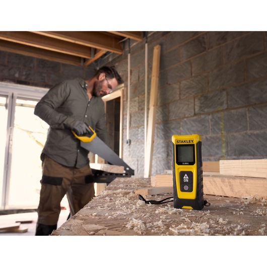 STANLEY STHT77065-0 laser distance measurer on workbench in woodworking workshop, yellow and black design.