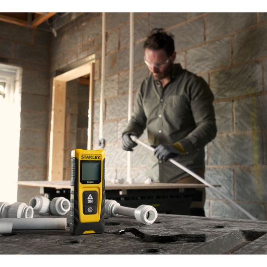 STANLEY STHT77065-0 laser distance measurer in workshop setting with pipes and fittings.