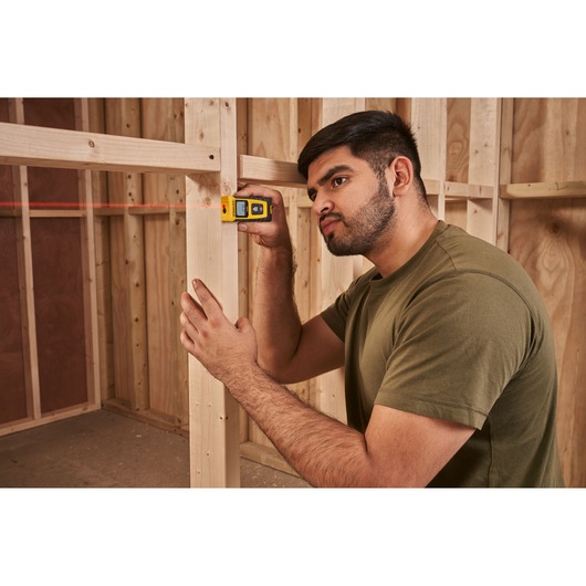 Photo of STANLEY STHT77065-0 laser distance measurer in use at a wood frame construction site.