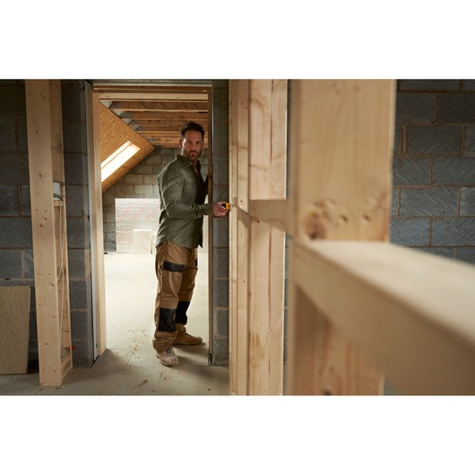 STANLEY STHT77065-0 photography of worker using tape measure in unfinished wooden framed room.