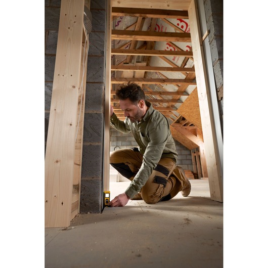 STANLEY STHT77065-0 laser distance measurer in use in a construction site, user measuring from floor to wall.