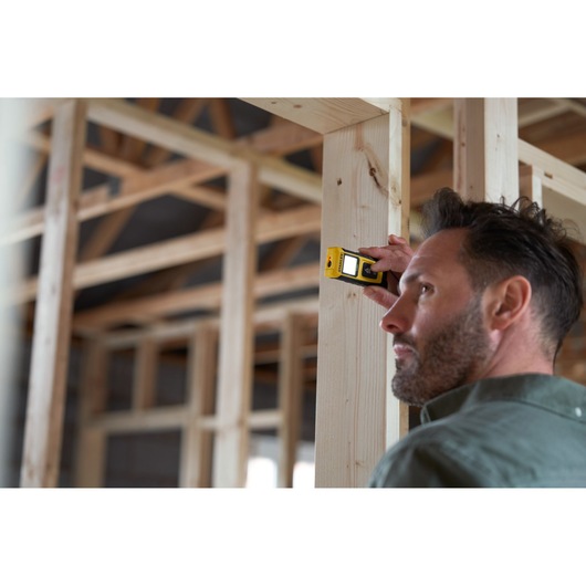 STANLEY STHT77065-0 digital laser measure used on wooden framing in construction site.