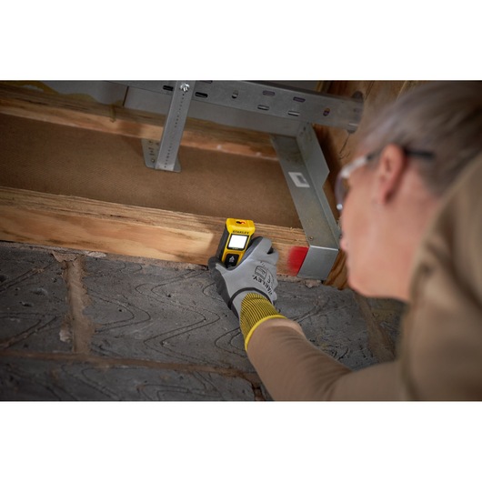 STANLEY STHT77065-0 stud finder used on wooden beam, close-up, user wearing gloves.