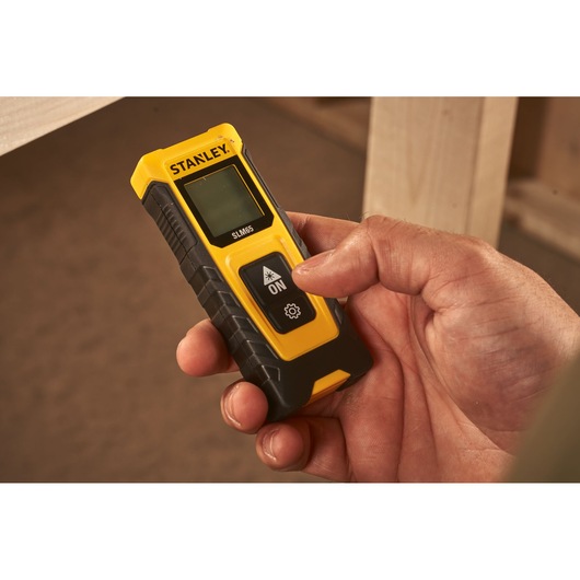 Photo of STANLEY STHT77065-0 digital laser distance measurer held in hand, black and yellow casing.