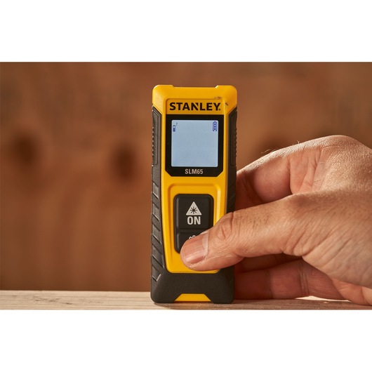 Photo of STANLEY STHT77065-0 laser distance measurer held by hand, yellow and black, close-up view.