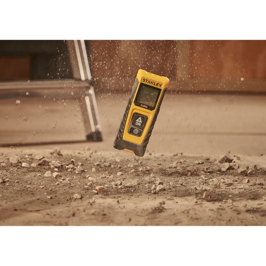STANLEY STHT77065-0 laser distance measurer in yellow and black, dropping onto a dusty floor.