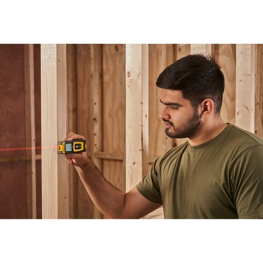 STANLEY STHT77100-0 laser distance measurer in use on wooden framing, handheld with visible red laser beam.