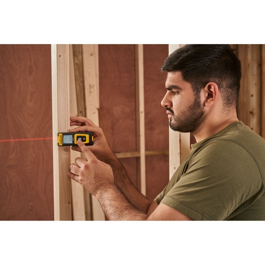 STANLEY STHT77100-0 laser distance measurer in use against wood framing, side angle.