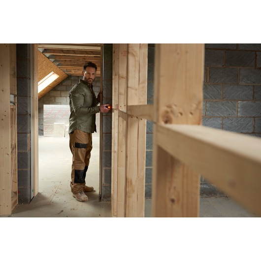 STANLEY STHT77100-0 laser measure used by worker in unfinished wooden-framed room, side angle photo.