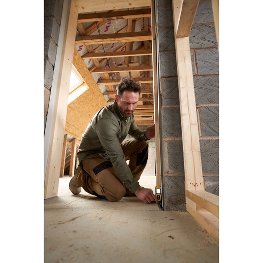 STANLEY STHT77100-0 laser distance measurer used by worker on construction site floor, angled front view.
