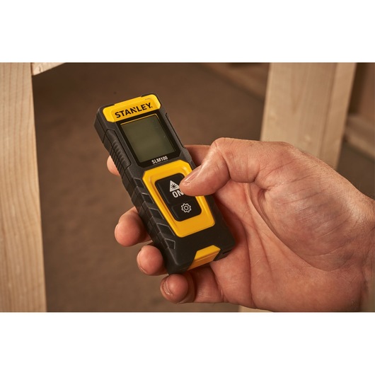 Photo of STANLEY STHT77100-0 digital laser distance measurer held in hand, black and yellow design.
