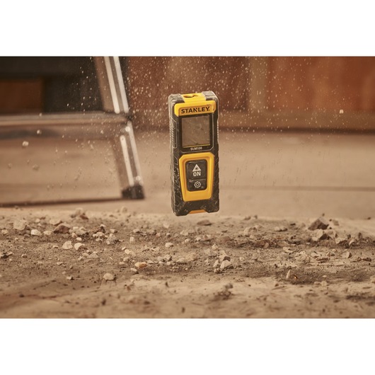 STANLEY STHT77100-0 laser distance measurer mid-air above dusty construction ground.