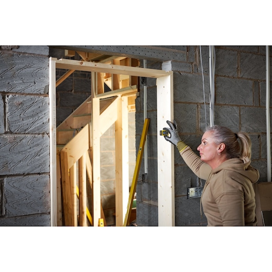 STANLEY STHT77666-0 laser distance measurer used by person on wooden door frame in construction site.