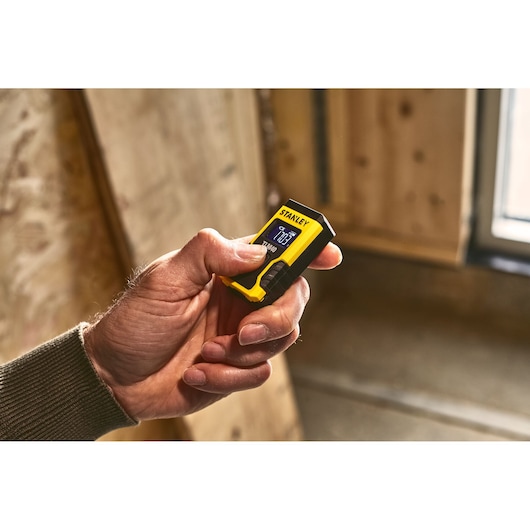 STANLEY STHT77666-0 compact yellow and black laser distance measurer in hand, indoor setting.