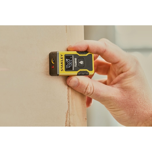 STANLEY STHT77666-0 laser distance measurer held against a wall, digital display visible.
