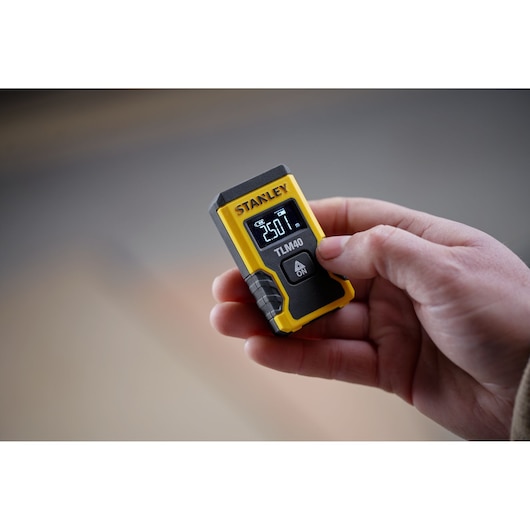 STANLEY STHT77666-0 laser distance measurer handheld, digital display, yellow and black, shown in use.