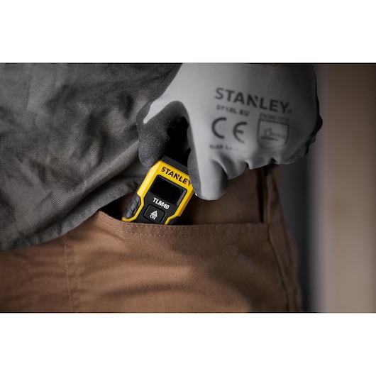 STANLEY STHT77666-0 laser measure being placed into pocket by gloved hand.