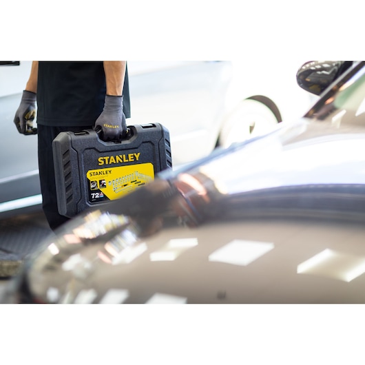 Photo of STANLEY STMT82829-1 socket set case held by person wearing gloves, near a car, angled view.