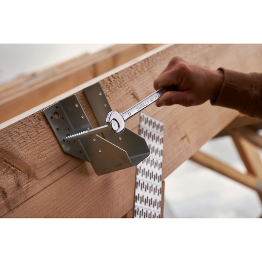 STANLEY STMT82832-1 combination wrench in use on metal bracket attached to wooden beam, outdoor setting.