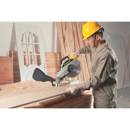 STANLEY STSM1510 miter saw used by worker cutting wooden plank in workshop, side view.
