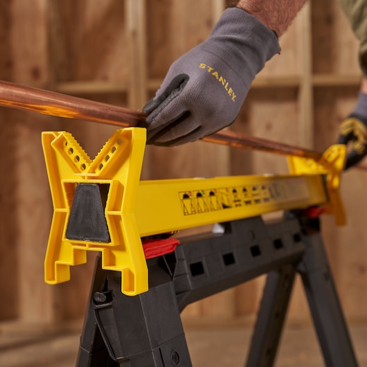 STANLEY STST1-70559 photography of yellow plastic saw horse holding copper pipe in workshop.