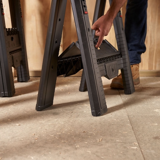 Photo of STANLEY STST1-70559 plastic sawhorse in use, black with support shelf, close-up angle.