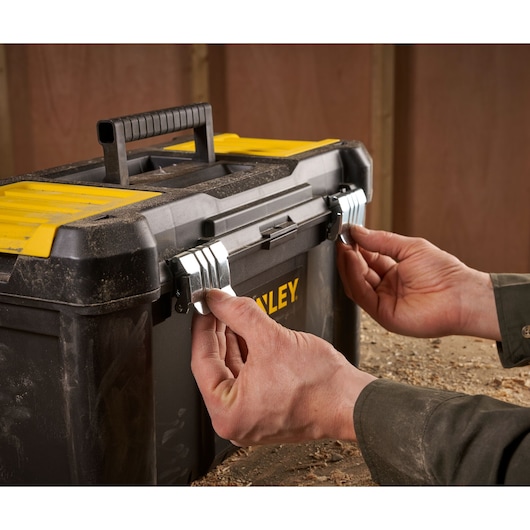 Stanley STST1-75521 toolbox with yellow lid, front view, hands securing metal latches, photo in workshop.