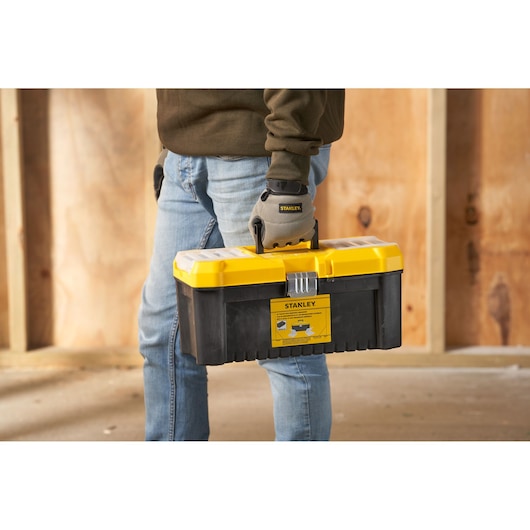 STANLEY STST75785-1 black and yellow toolbox carried by person wearing work gloves, photography side view.