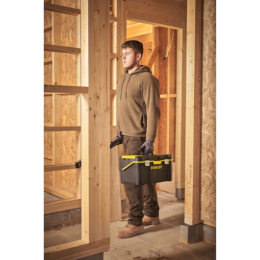 Photo of a person holding a STANLEY STST83397-1 tool box, black with yellow accents, at a construction site.