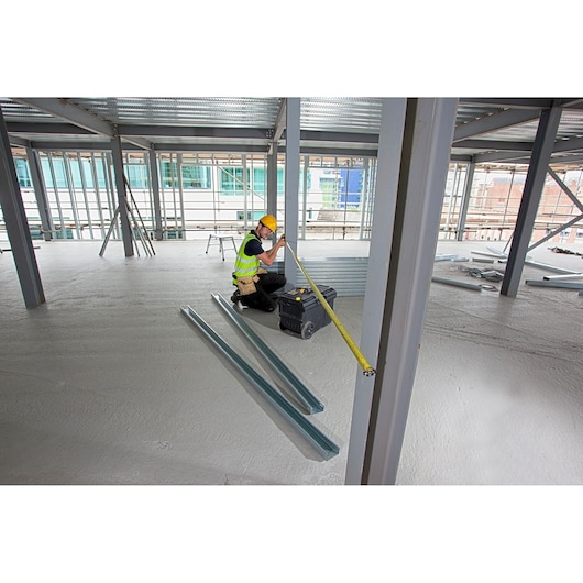 STANLEY XTHT0-33504 tape measure in use by worker measuring steel beam at construction site, wide angle.