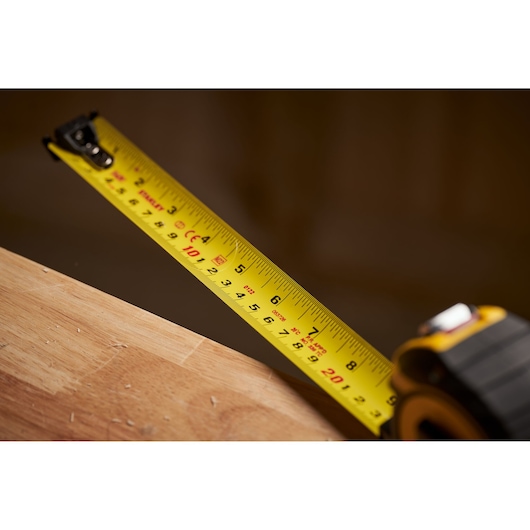 STANLEY XTHT0-33504 tape measure extended on wood surface, close-up, photography product image.