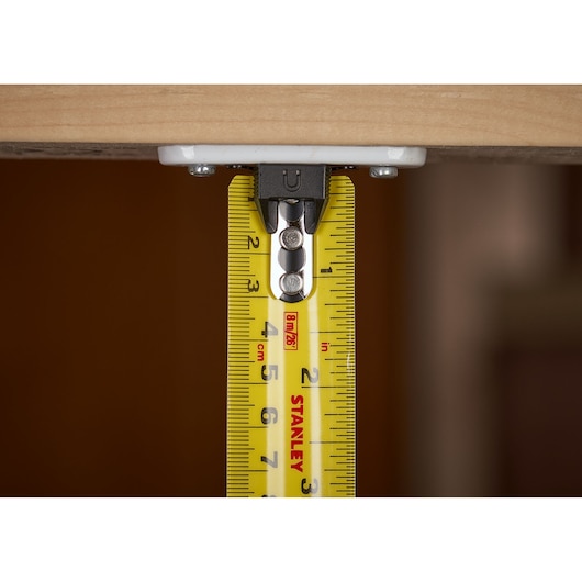 STANLEY XTHT0-33504 tape measure close-up showing metric markings and hook under wood, product photography.
