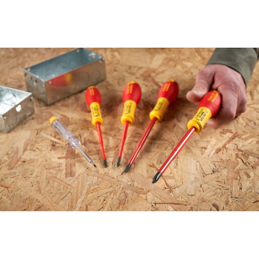 STANLEY XTHT0-62692 insulated screwdriver set with red and yellow handles on a wooden surface, hand holding one tool.